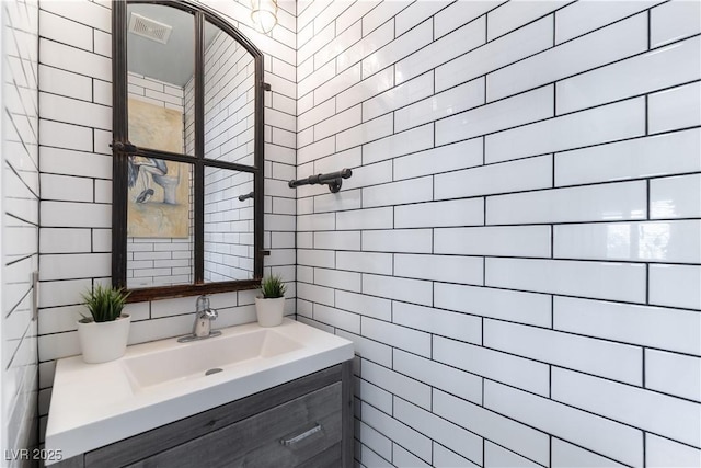 bathroom featuring tile walls, backsplash, vanity, and visible vents