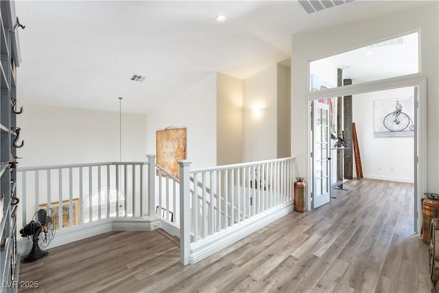 hall with baseboards, visible vents, wood finished floors, and an upstairs landing