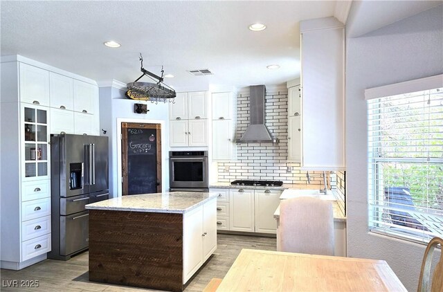 kitchen with visible vents, wall chimney exhaust hood, white cabinets, backsplash, and stainless steel appliances