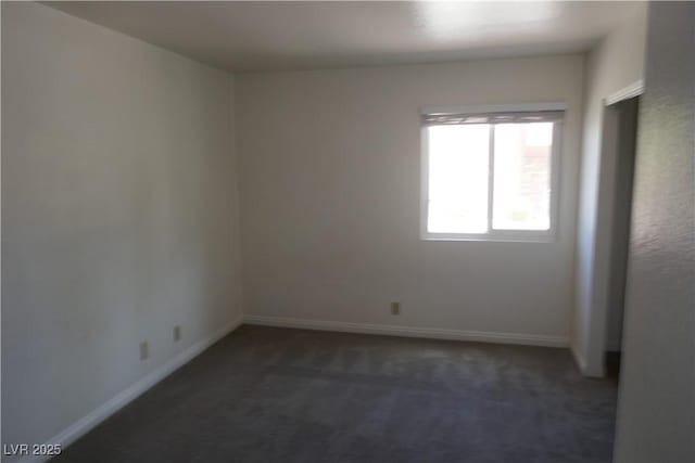 spare room featuring dark colored carpet and baseboards