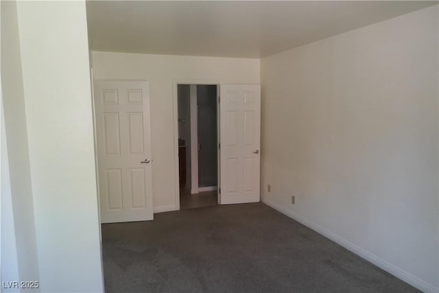 spare room with baseboards and dark colored carpet