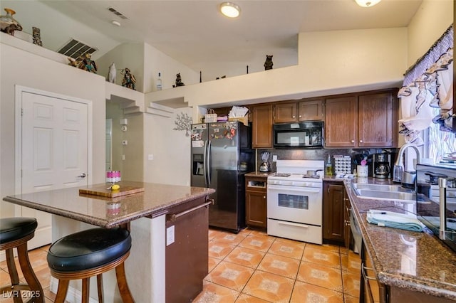 kitchen with decorative backsplash, a sink, light tile patterned floors, black appliances, and dark stone countertops