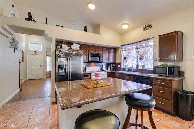 kitchen with a sink, a kitchen breakfast bar, light tile patterned floors, vaulted ceiling, and black appliances