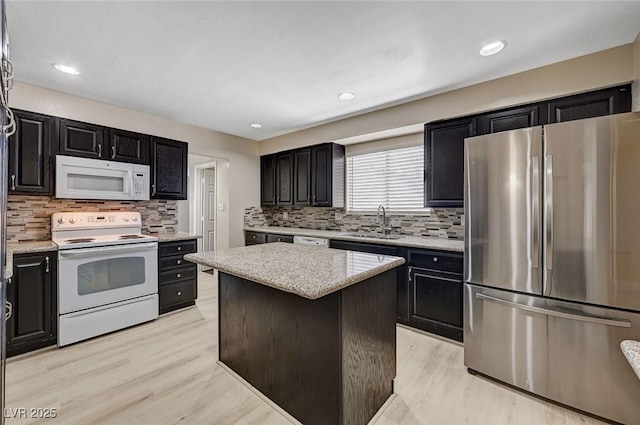 kitchen with white appliances, tasteful backsplash, a sink, and light wood-style floors