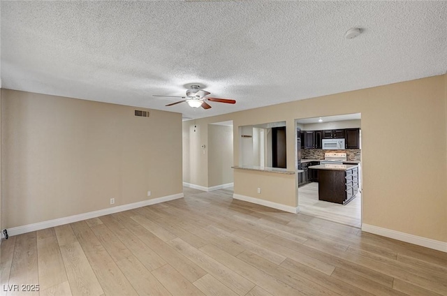 unfurnished living room featuring ceiling fan, light wood-style floors, a textured ceiling, baseboards, and visible vents