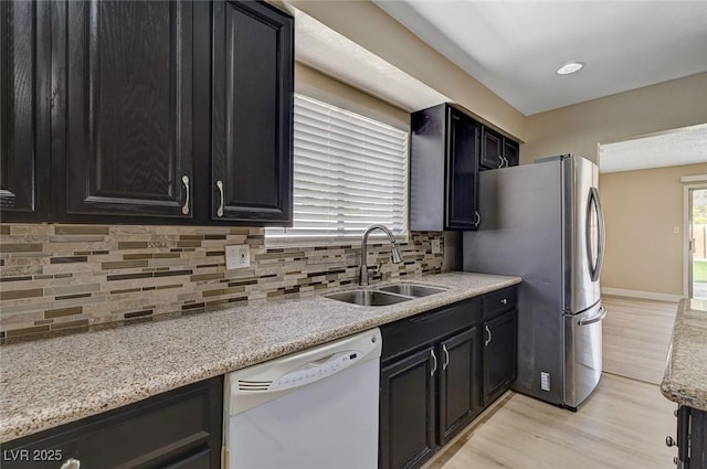 kitchen with dark cabinetry, white dishwasher, a sink, and light wood-style floors