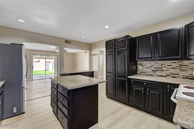 kitchen with dark cabinets, freestanding refrigerator, light wood-style flooring, and visible vents