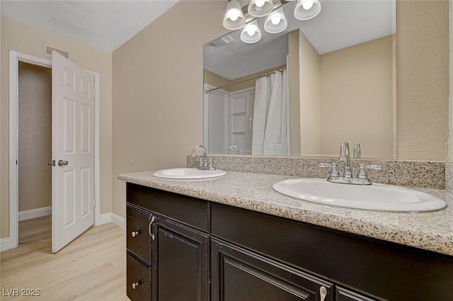 full bath with double vanity, a sink, baseboards, and wood finished floors