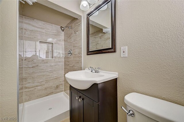 full bathroom with vanity, a textured wall, toilet, and tiled shower