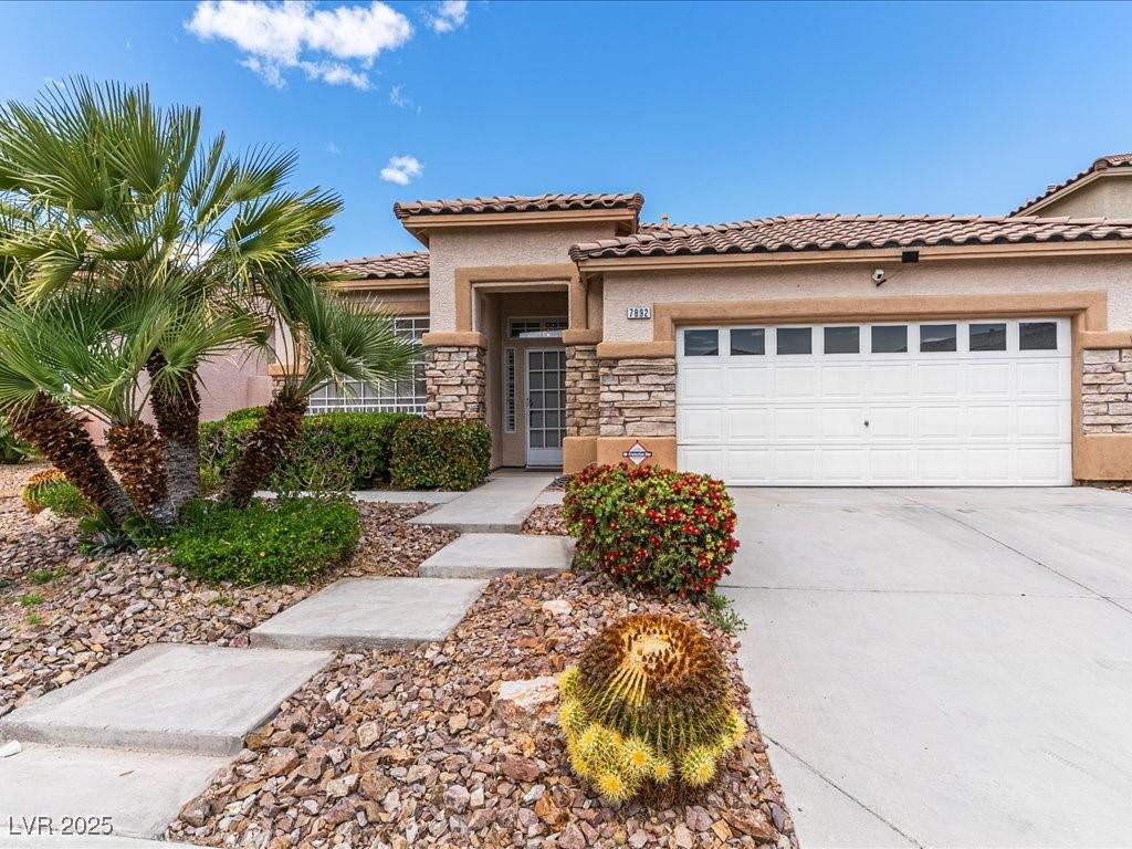 mediterranean / spanish house with an attached garage, driveway, stone siding, and stucco siding