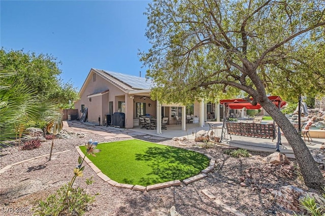 rear view of property featuring roof mounted solar panels, fence, a patio, and stucco siding