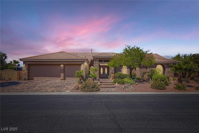 ranch-style house featuring an attached garage, stucco siding, a gate, decorative driveway, and french doors