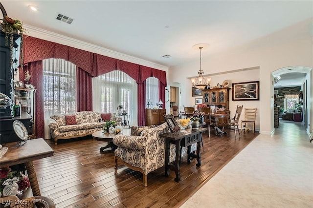 living room with visible vents, ornamental molding, wood finished floors, a chandelier, and arched walkways