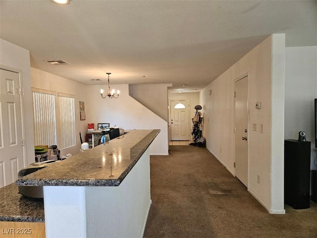 kitchen with visible vents, dark countertops, dark colored carpet, a notable chandelier, and hanging light fixtures