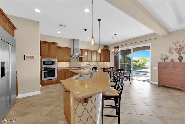 kitchen with a breakfast bar, a sink, an island with sink, wall chimney exhaust hood, and stainless steel appliances