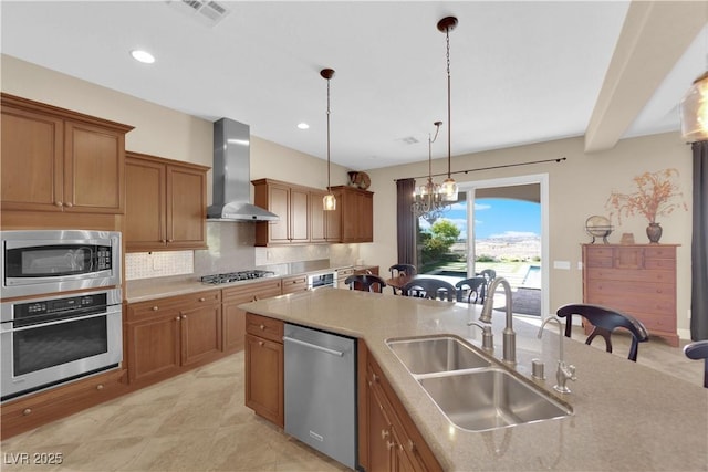 kitchen with backsplash, visible vents, appliances with stainless steel finishes, a sink, and wall chimney exhaust hood
