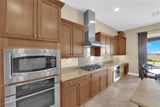 kitchen with wall chimney range hood, backsplash, visible vents, light countertops, and stainless steel appliances