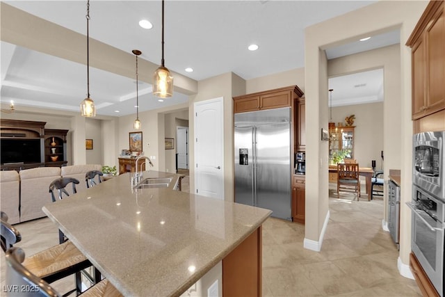 kitchen featuring a breakfast bar, a sink, built in appliances, recessed lighting, and a center island with sink