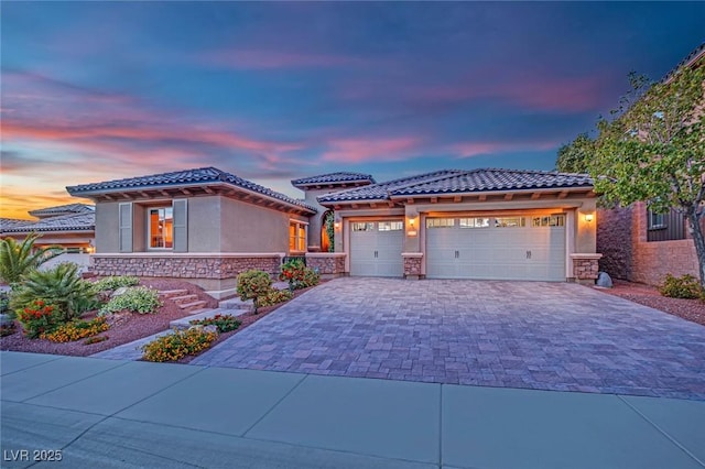 view of front of home with a tiled roof, decorative driveway, an attached garage, and stucco siding