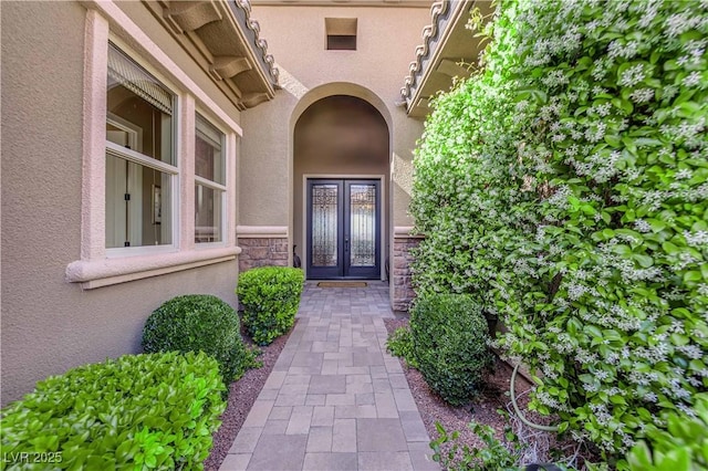 property entrance featuring french doors, stone siding, and stucco siding