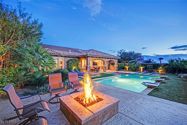pool at dusk featuring a fire pit, an outdoor pool, and a patio area