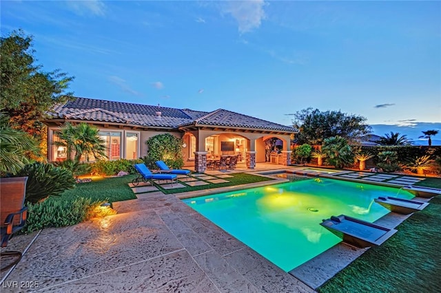 pool at dusk with a fenced in pool, an in ground hot tub, and a patio area