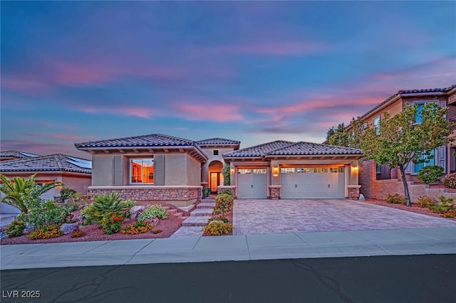 mediterranean / spanish-style home featuring a garage, decorative driveway, stucco siding, and a tile roof