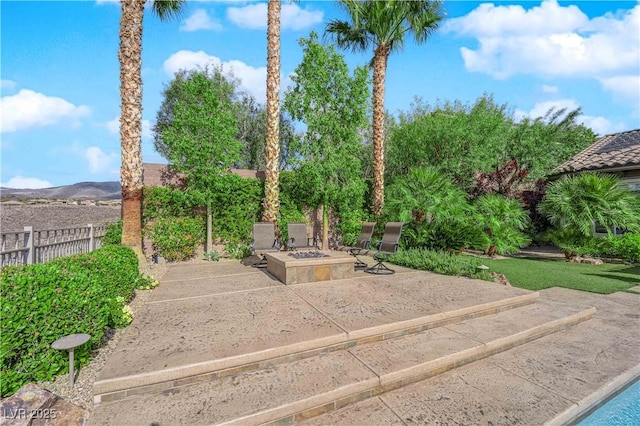 view of patio with fence, a mountain view, and an outdoor fire pit