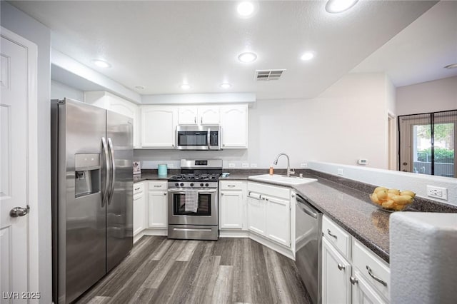 kitchen with appliances with stainless steel finishes, a sink, dark wood finished floors, white cabinetry, and visible vents
