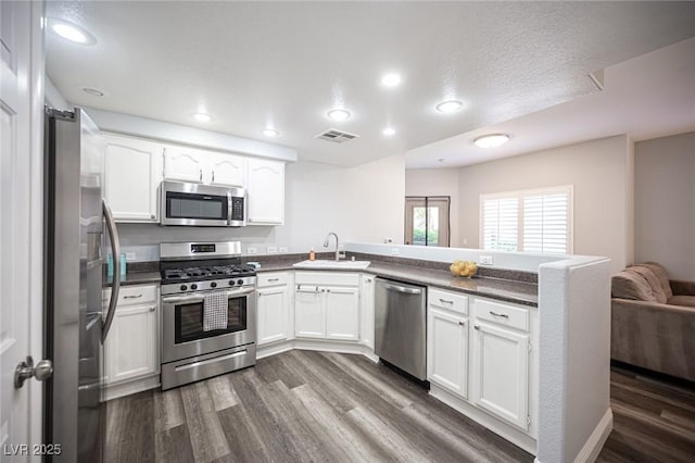 kitchen featuring visible vents, a peninsula, dark countertops, a sink, and stainless steel appliances