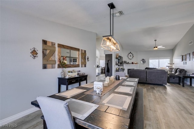 dining space with a ceiling fan, visible vents, wood finished floors, and a fireplace