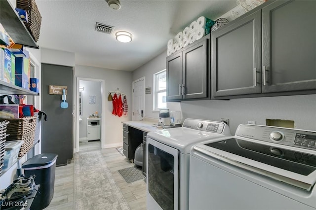 clothes washing area featuring visible vents, washing machine and clothes dryer, cabinet space, baseboards, and light wood finished floors