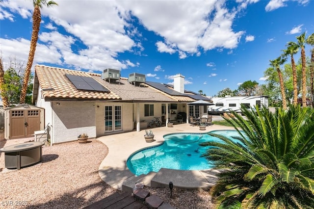 rear view of property featuring a tiled roof, a patio area, roof mounted solar panels, a storage unit, and stucco siding