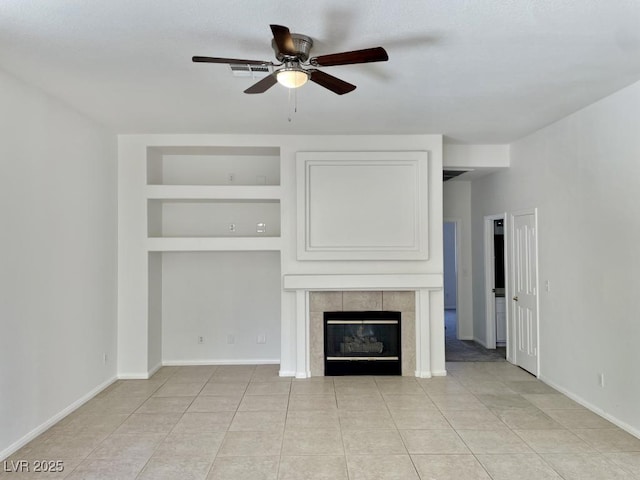 unfurnished living room featuring built in features, light tile patterned flooring, baseboards, a tiled fireplace, and a ceiling fan