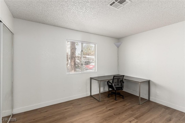 unfurnished office featuring visible vents, a textured ceiling, and wood finished floors