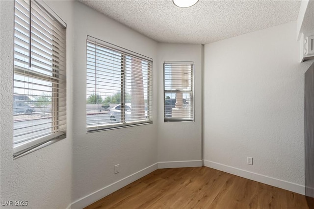 unfurnished room featuring a textured ceiling, a textured wall, baseboards, and light wood-style floors