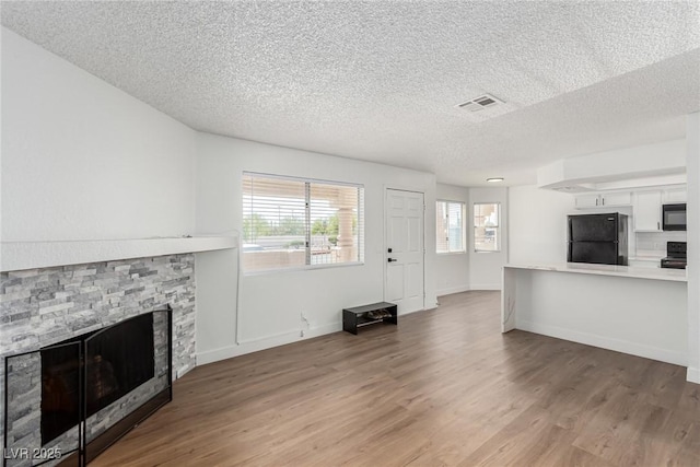 unfurnished living room with a stone fireplace, a textured ceiling, light wood finished floors, and a healthy amount of sunlight