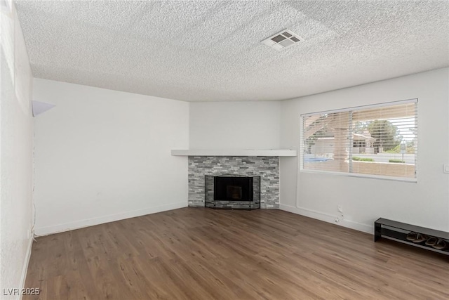 unfurnished living room with visible vents, a textured ceiling, wood finished floors, and a fireplace