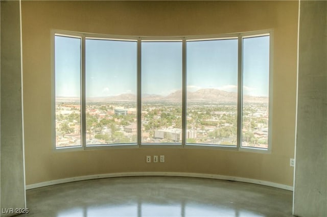 empty room with baseboards, plenty of natural light, concrete flooring, and a mountain view