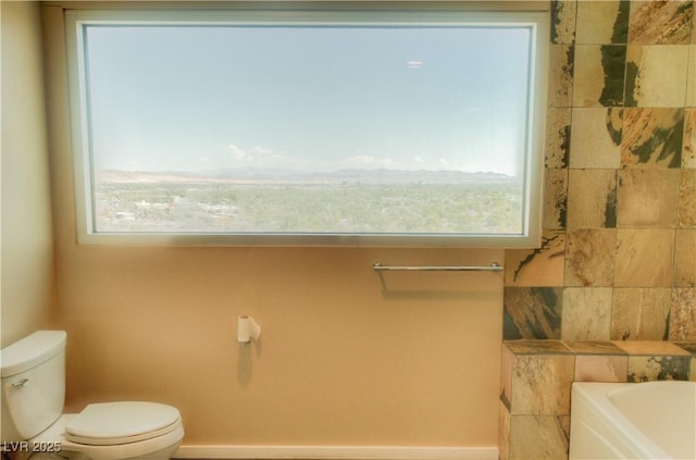 bathroom with baseboards, a garden tub, toilet, and a wealth of natural light