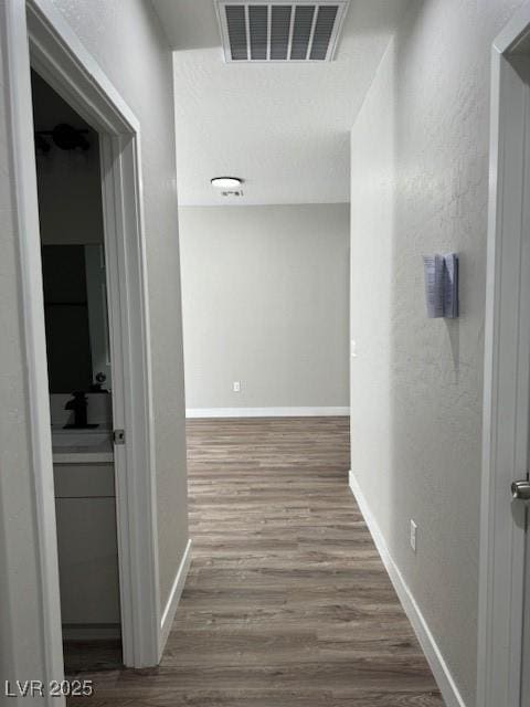 hall featuring baseboards, visible vents, and wood finished floors