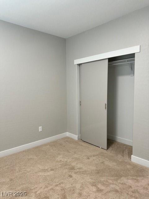 unfurnished bedroom featuring baseboards, light colored carpet, and a closet