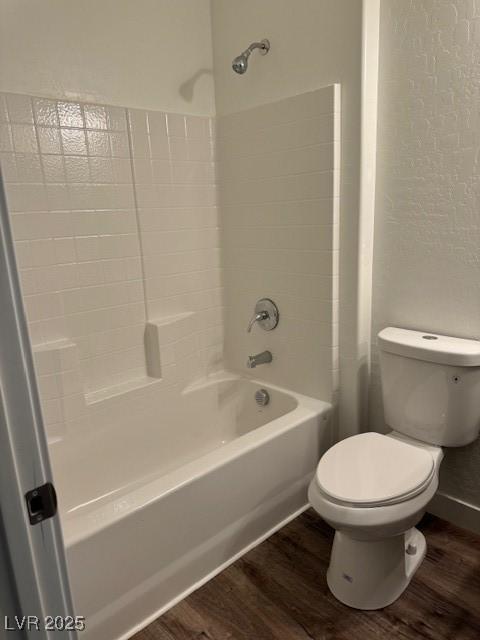 bathroom featuring toilet, wood finished floors, and shower / bathing tub combination