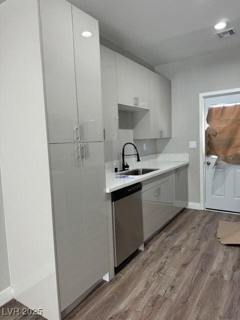 kitchen featuring stainless steel dishwasher, light wood-type flooring, a sink, light countertops, and baseboards