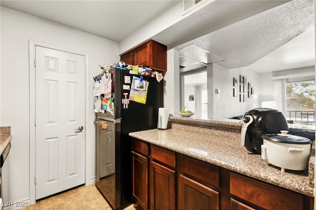 kitchen with light tile patterned flooring, light stone countertops, freestanding refrigerator, open floor plan, and visible vents