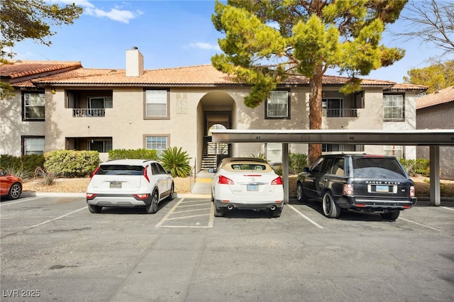 view of front of property featuring covered and uncovered parking, a chimney, a tile roof, and stucco siding