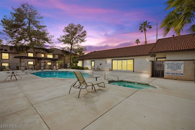 pool at dusk featuring a hot tub, outdoor dry bar, a community pool, and a patio area