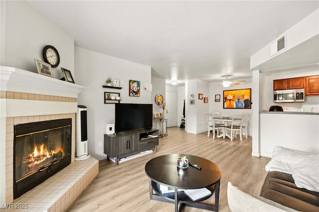 living room with visible vents, ceiling fan, a glass covered fireplace, and light wood finished floors