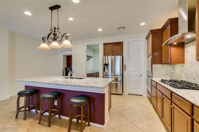 kitchen with backsplash, appliances with stainless steel finishes, a center island with sink, a sink, and wall chimney exhaust hood
