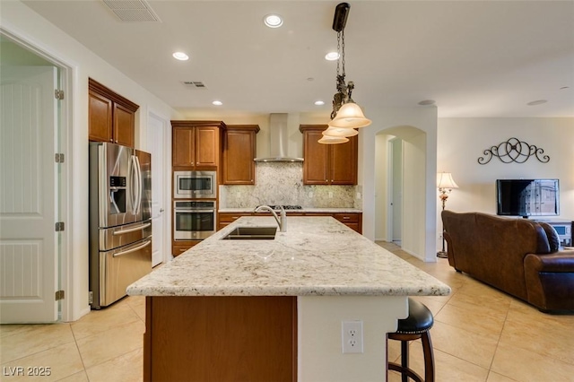 kitchen featuring wall chimney range hood, visible vents, appliances with stainless steel finishes, arched walkways, and a sink